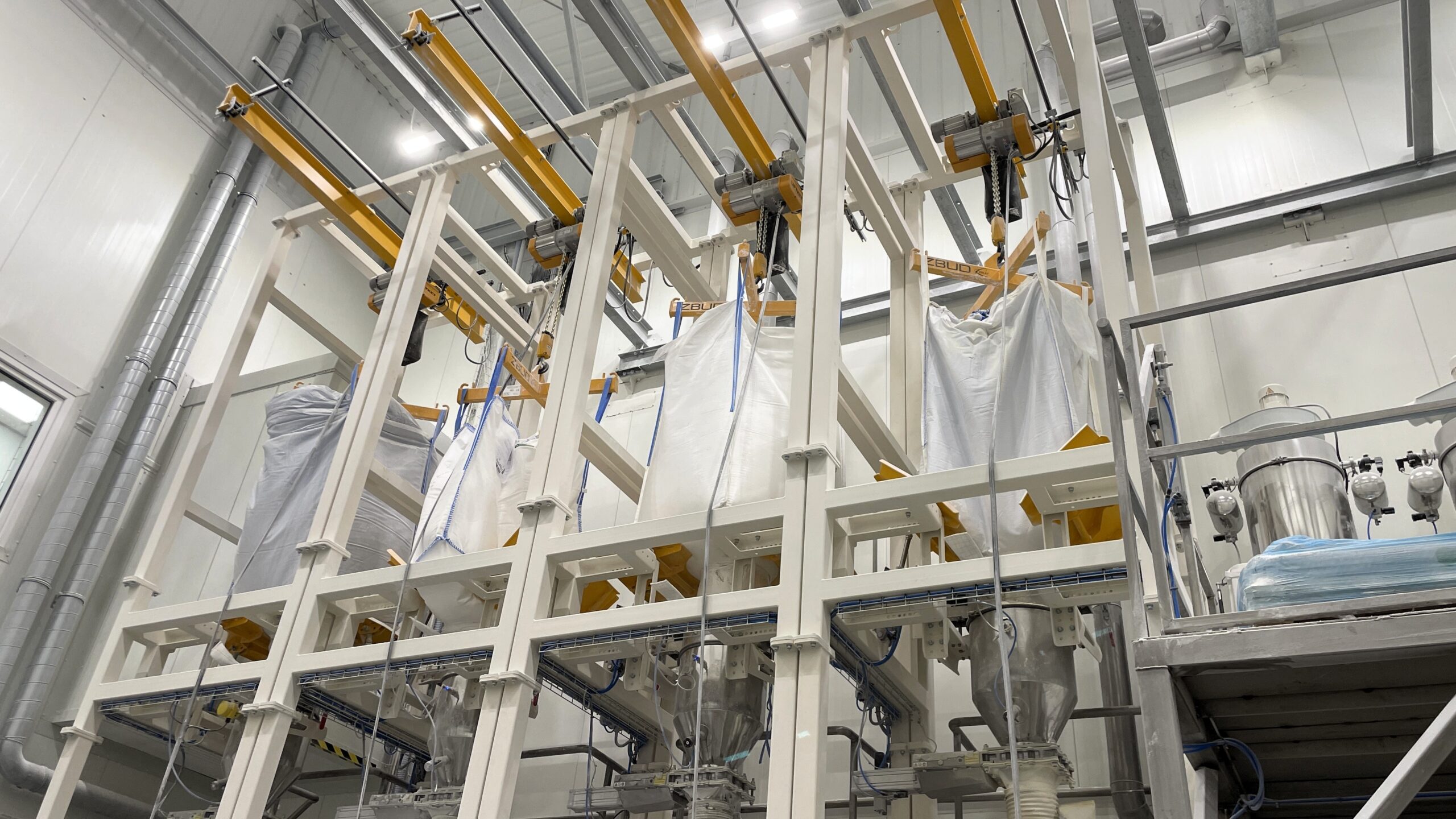 Four big bag emptying stations with electric hoists above feeders at a food production plant